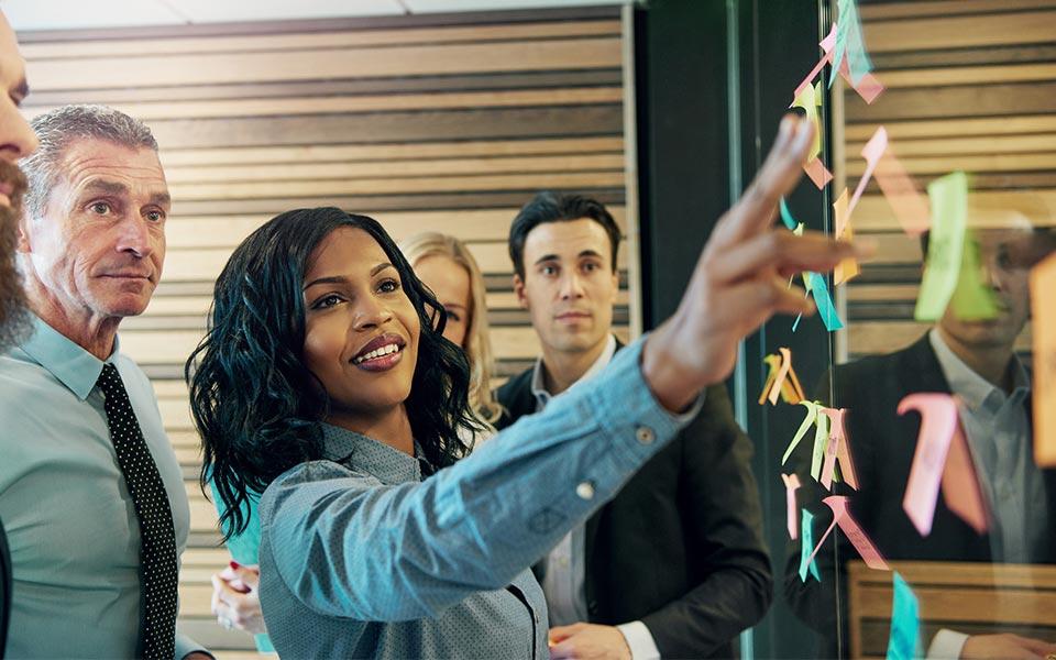 Team watches as leader points to board covered in colorful sticky notes